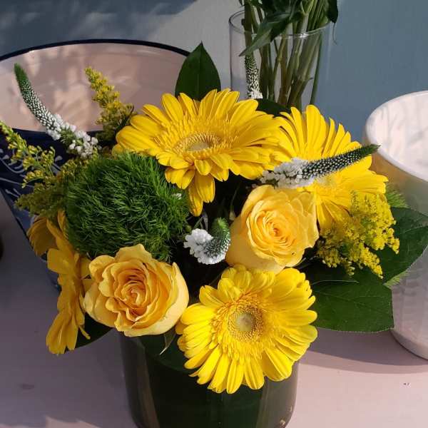 Compact yellow gerbera daisy and rose arrangement in a short glass vase