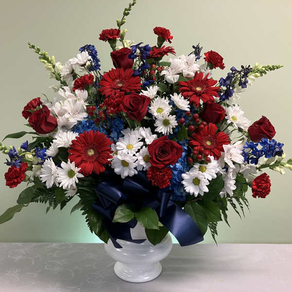 Patriotic red, white and blue flower arrangement in a white urn with a navy bow.