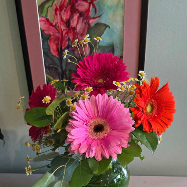 Bright pink and orange gerbera daisies with small white daisies in a clear glass vase.