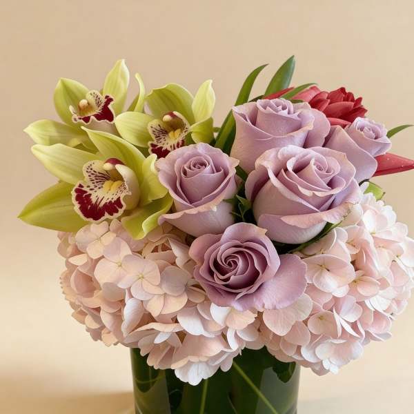 Low arrangement of lavender roses, green orchids, and blush hydrangeas in a glass vase