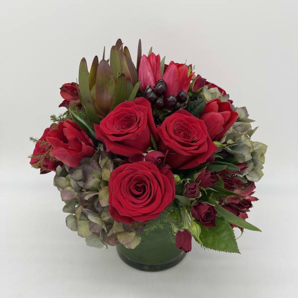 Low round arrangement of red roses with mixed hydrangeas in a glass vase