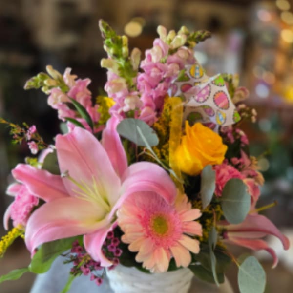 Pink lilies, gerbera daisy, and a yellow rose in a white woven basket with pastel accents