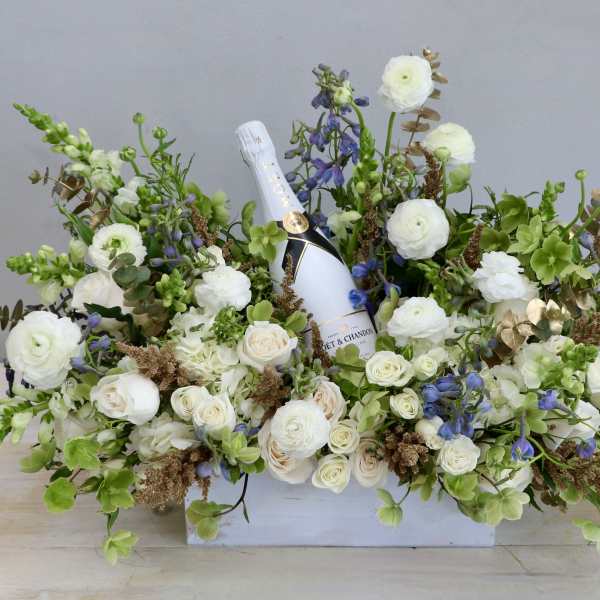 Low white box arrangement of white and green flowers with a champagne bottle nestled in the center