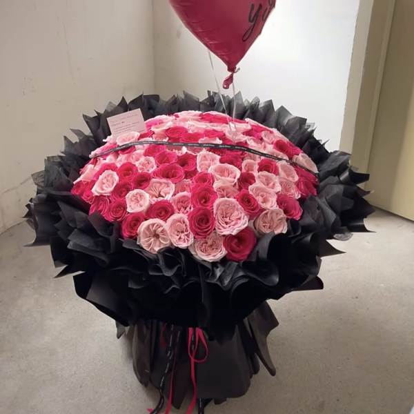 Large bouquet of pink and red roses wrapped in black paper with a red heart balloon that says I love you.