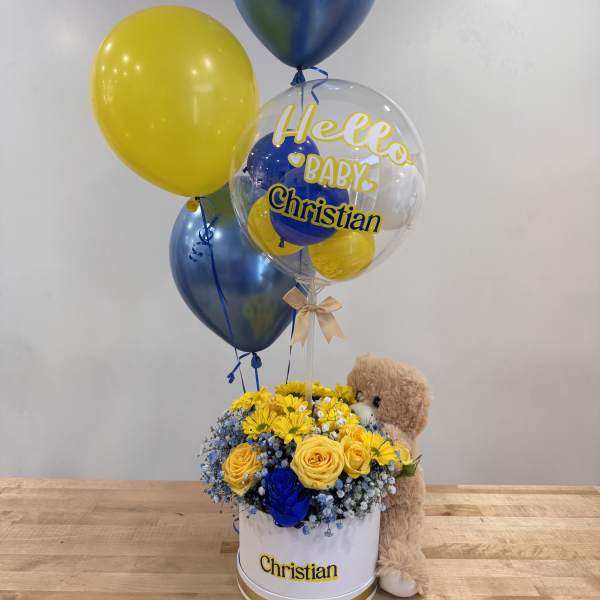 Blue and yellow flower hat box with baby-themed balloons and a teddy bear.
