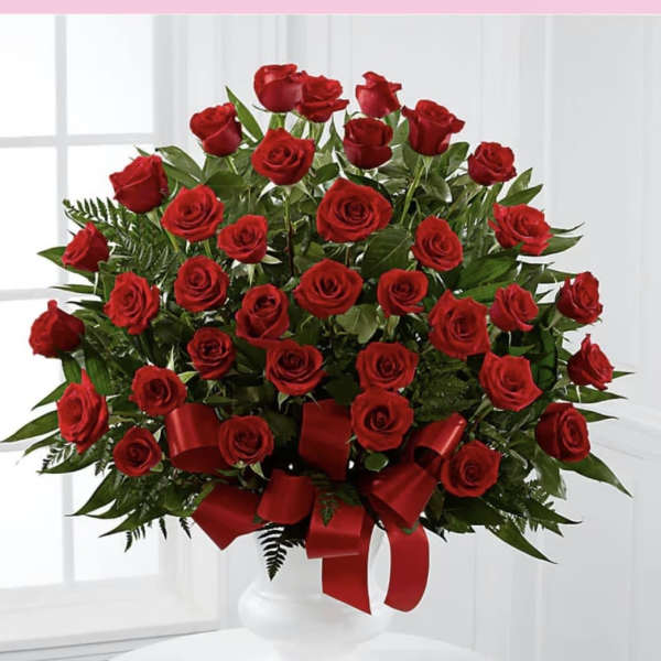 Large arrangement of red roses with red ribbon in a white pedestal vase