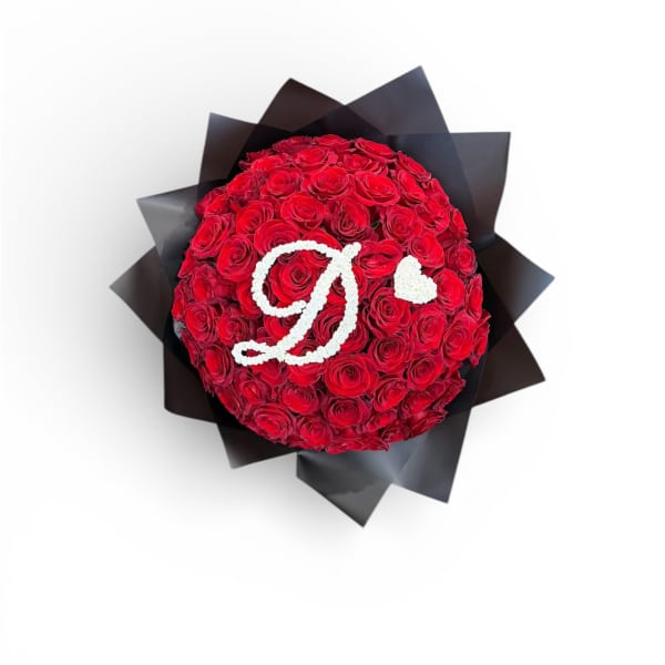 Round bouquet of red roses with white flowers forming a letter D and heart, wrapped in black paper.