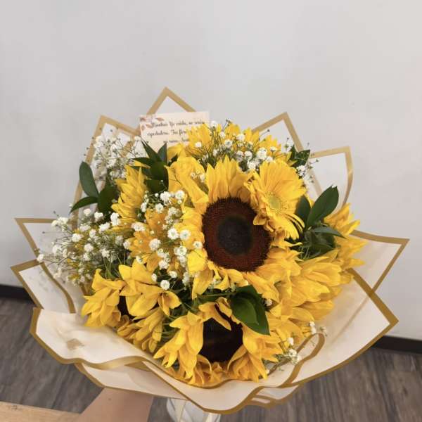 Hand-tied bouquet of bright yellow sunflowers and tiny white blooms wrapped in cream and gold paper