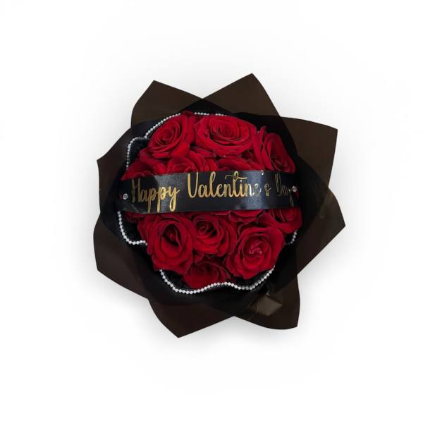Round bouquet of red roses wrapped in black paper with a Happy Valentine’s Day ribbon and pearl accents.