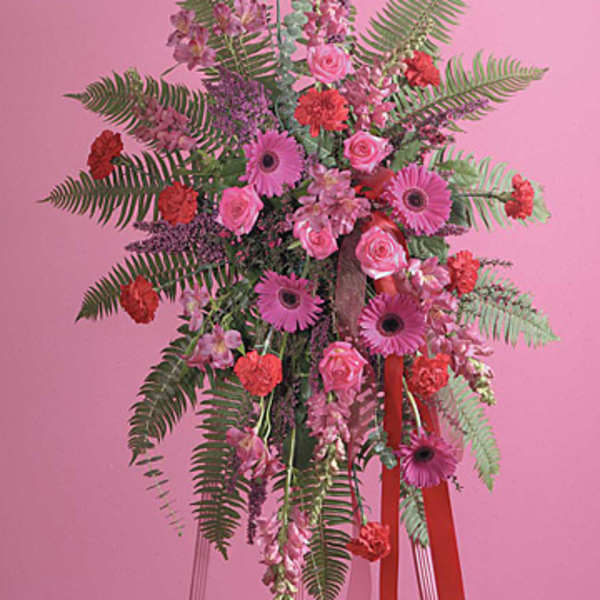 Tall pink and red standing spray with gerbera daisies, roses, carnations, and ferns on an easel.