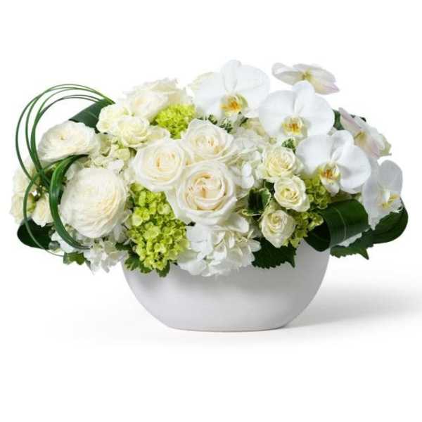 Low white bowl of white roses, hydrangeas, and orchids with light green accents.