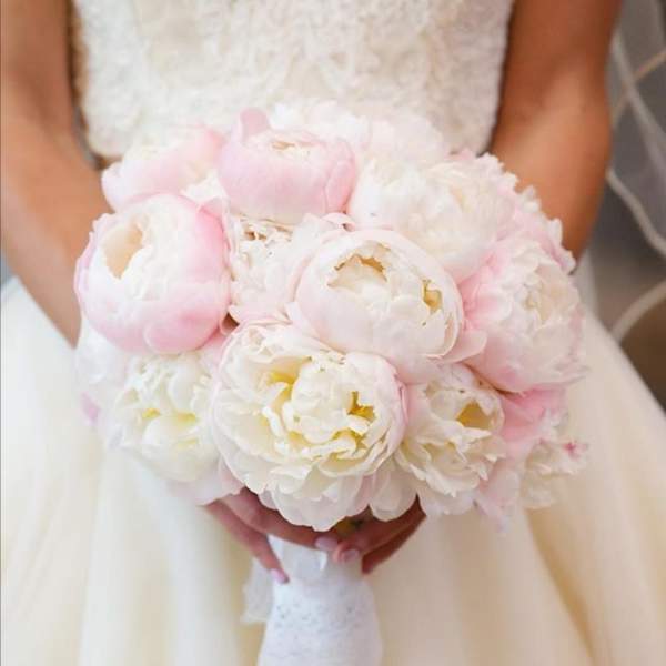 Round bridal bouquet of white and pale pink peonies wrapped with white lace