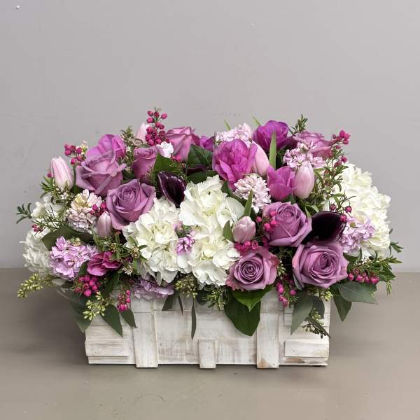 Low rectangular arrangement of pink and purple flowers with white blooms in a white wooden box