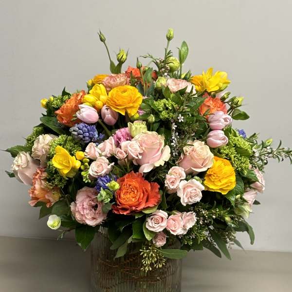 Colorful arrangement of pink roses and mixed bright blooms in a ribbed glass cylinder vase