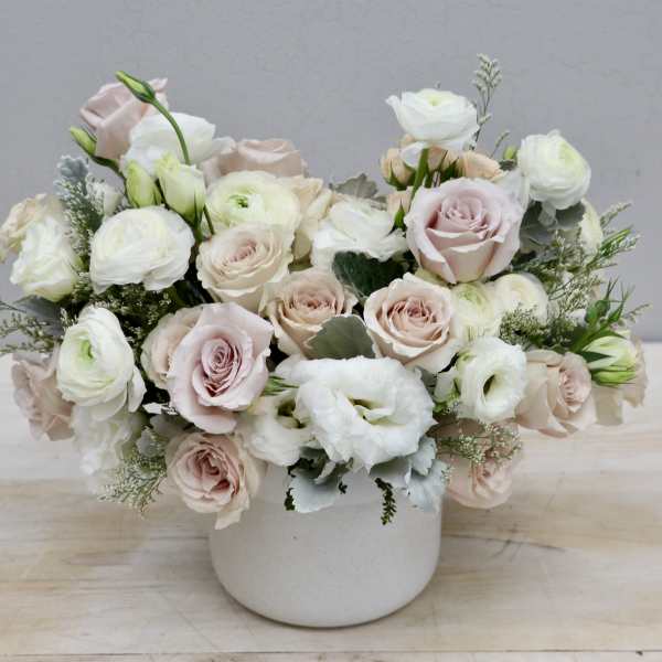 Low arrangement of blush roses and white ranunculus in a matte white ceramic pot