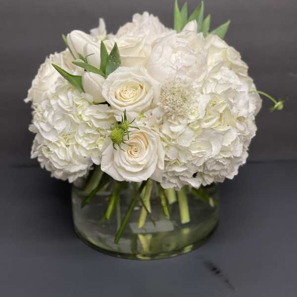 Low round arrangement of white roses, hydrangeas, and peonies in a clear glass vase