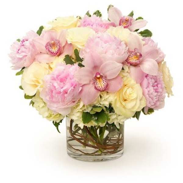 Low arrangement of pink peonies, pale orchids, and cream roses in a clear glass vase.