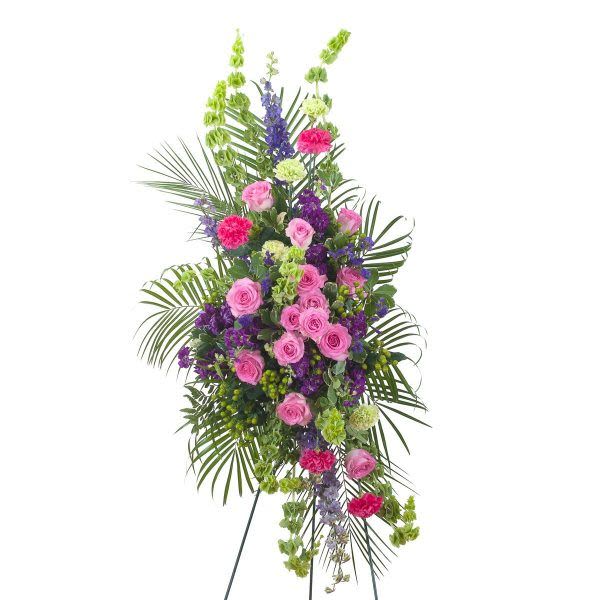 Tall standing spray of pink roses and carnations with purple flowers and palms on an easel