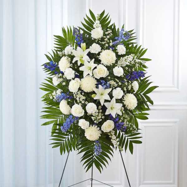 Standing spray of white lilies, roses, and mums with blue flowers on an easel