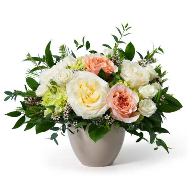 Low arrangement of white and peach roses with pale blooms in a round ceramic vase