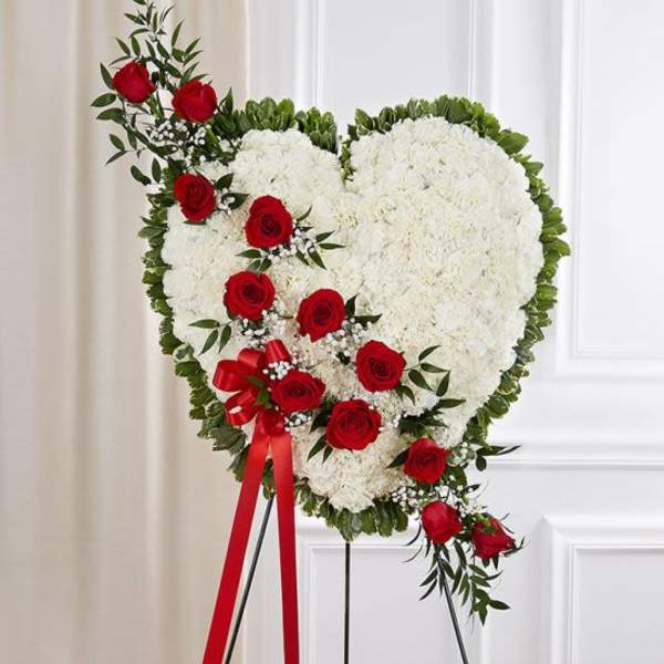 Heart-shaped white floral standing wreath with red roses on an easel.