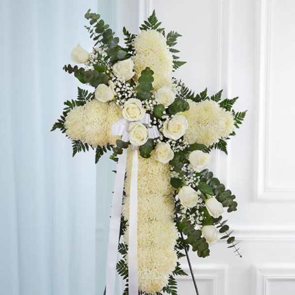 Tall white floral cross with roses and ribbon on a stand for a memorial display