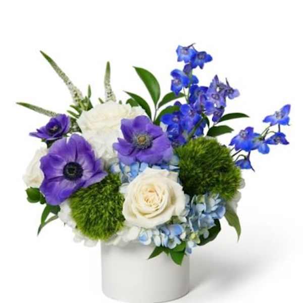 Compact blue and purple flower arrangement with white roses in a white ceramic cylinder vase