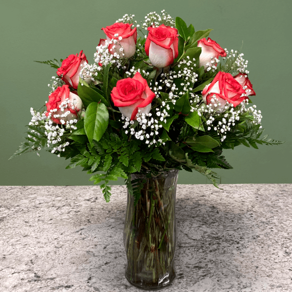 Vase arrangement of red and white roses with baby's breath in a clear glass vase on a stone countertop