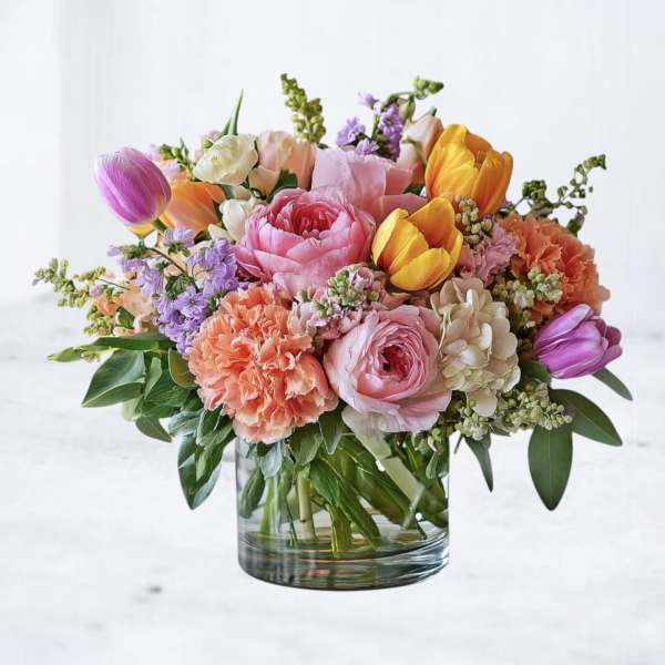 Low glass vase of pink peonies, peach carnations, yellow and purple tulips with pastel filler flowers
