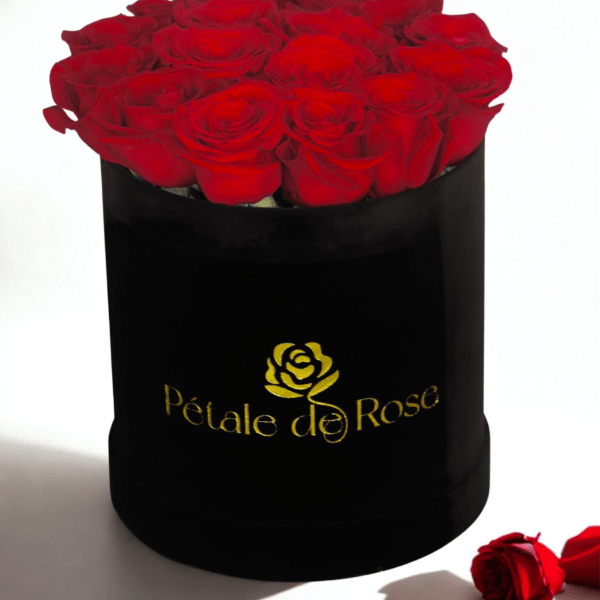 Round black hat box filled with tightly packed red roses with a gold logo on the front.
