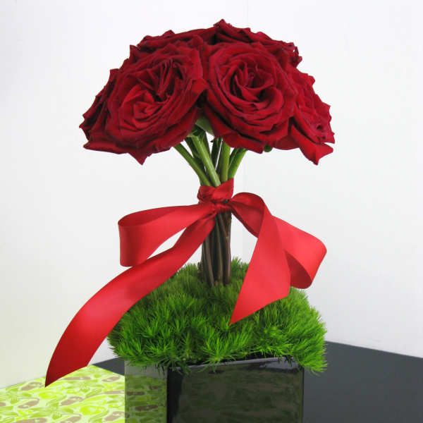 Topiary-style arrangement of red roses in a black cube vase with a red ribbon bow