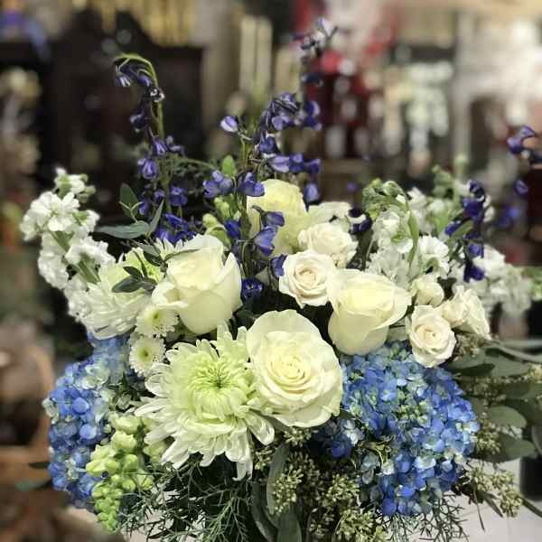 White roses, blue hydrangeas, and purple delphinium in a clear glass vase