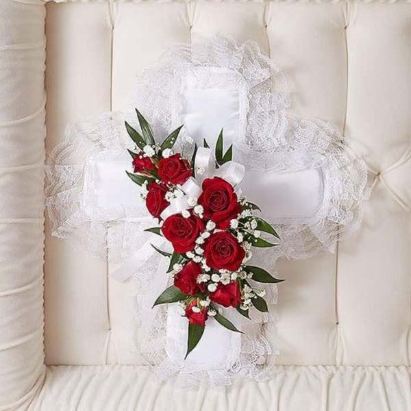 White fabric cross with red roses and white accent flowers inside a cream casket interior.