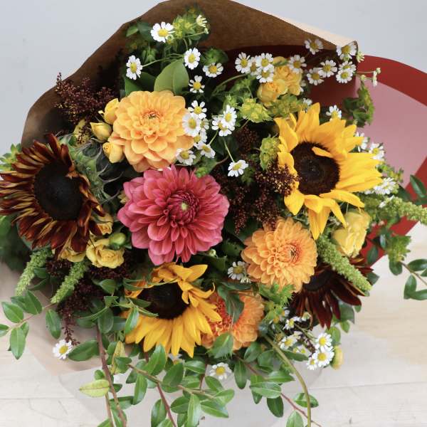 Bright bouquet with sunflowers, dahlias, spray roses, and small daisies wrapped in brown paper