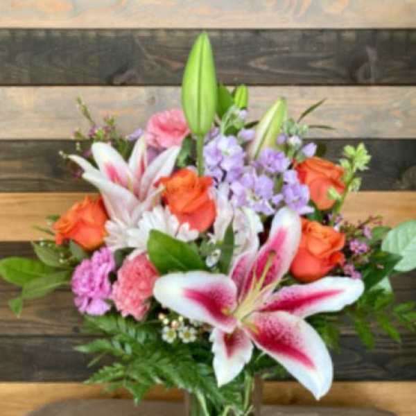 Tall mixed bouquet with pink lilies, orange roses, pink carnations and white daisies in a glass vase