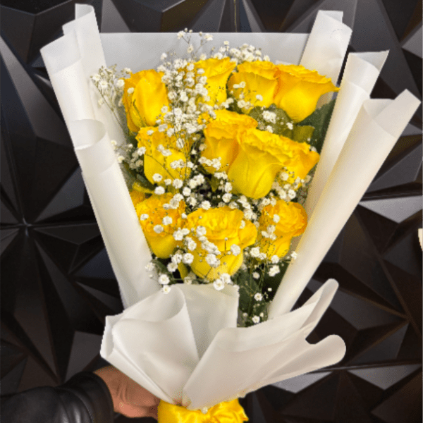 Bouquet of yellow roses with white filler flowers wrapped in white paper and tied with a yellow ribbon