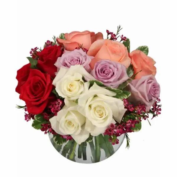 Round arrangement of red, white, peach, and lavender roses in a clear glass bowl vase