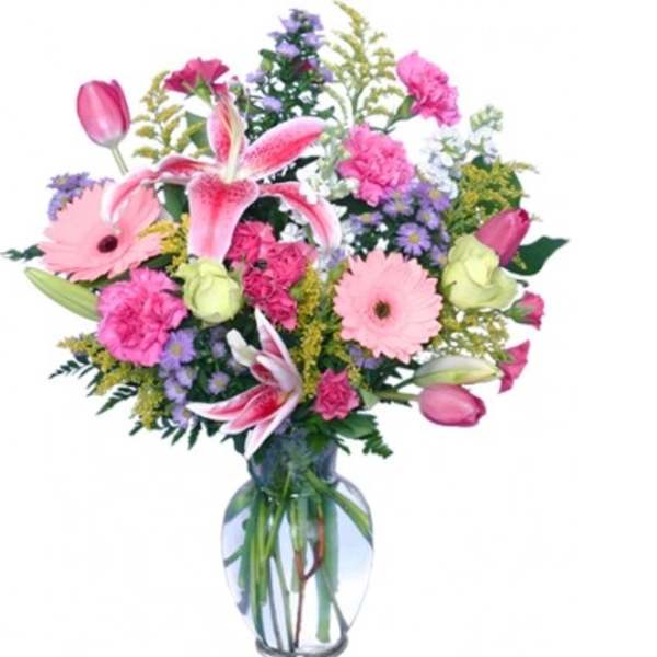 Mixed bouquet of pink lilies, tulips, carnations, and daisies in a clear glass vase