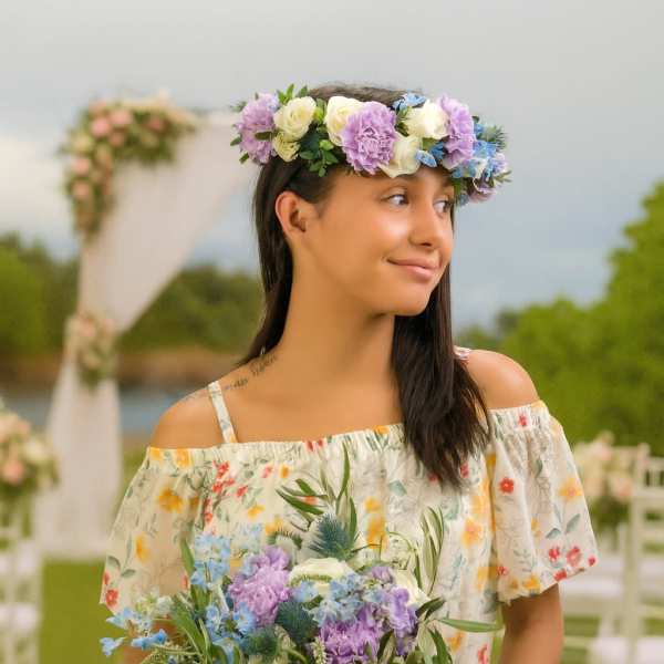 Woman holding a purple, blue, and white bouquet and wearing a matching floral crown outdoors