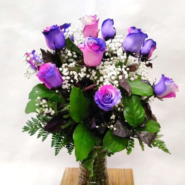 Arrangement of pink and purple roses with white filler flowers in a clear glass vase