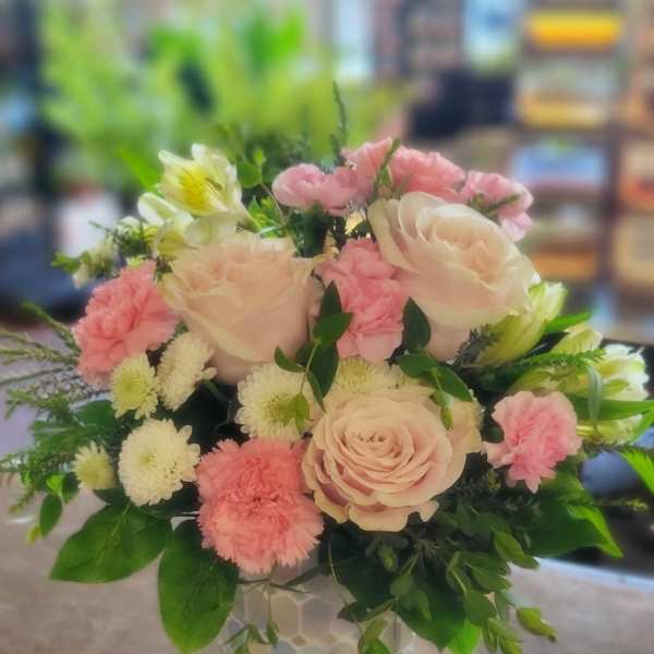 Round arrangement of pale pink roses, pink carnations, and white mums in a patterned ceramic vase
