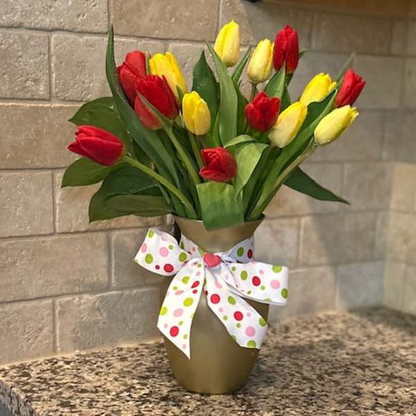 Red and yellow tulips in a gold vase with a white polka dot bow on a countertop