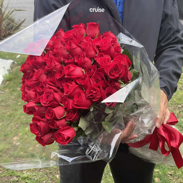 Large bouquet of dozens of red roses wrapped in clear cellophane with a red ribbon