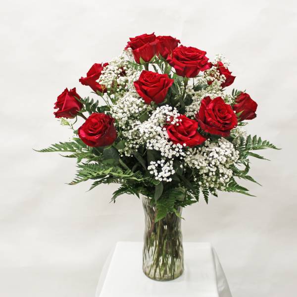 Tall arrangement of red roses and white filler flowers in a clear glass vase