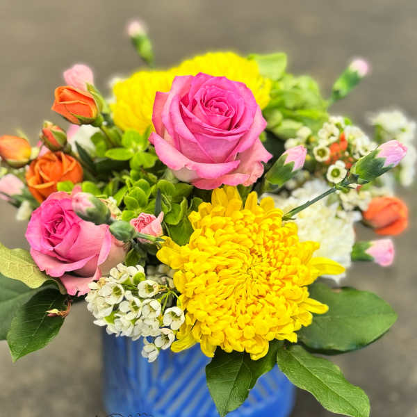 Bright mixed bouquet of pink roses, yellow mums, and small white blooms in a blue ceramic vase
