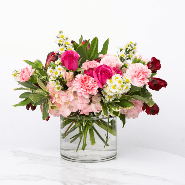 Pink roses, carnations, hydrangea, and white daisies in a clear glass vase