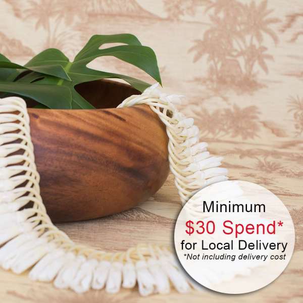 Wooden bowl with a green tropical leaf and white shell lei draped over the rim.