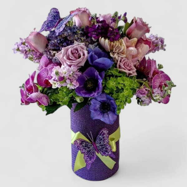 Purple and pink bouquet with roses, anemones, and orchids in a purple vase with butterfly decorations