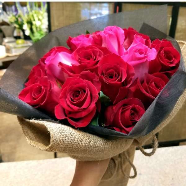 Hand-tied bouquet of red and pink roses wrapped in black paper and burlap