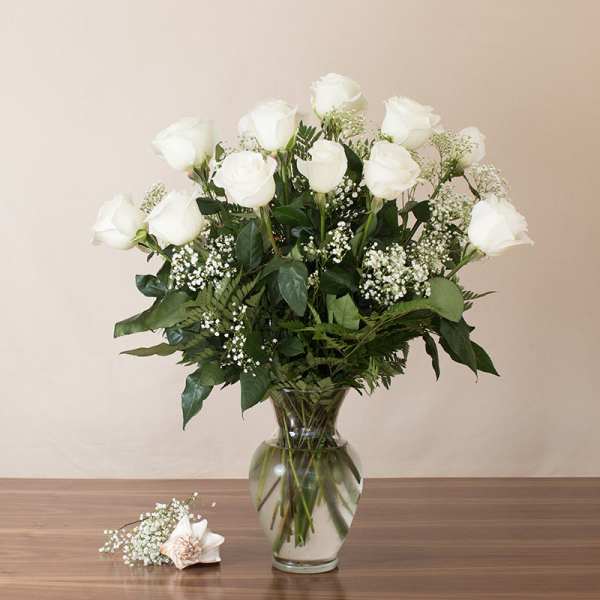 Tall arrangement of white roses and baby's breath in a clear glass vase on a wooden table